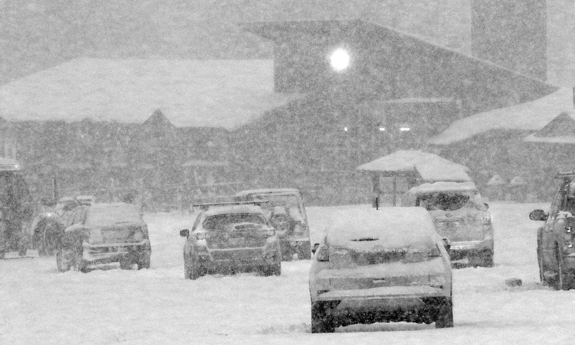 A black and white image of the Mt. Mansfield Base Lodge and cars in the parking lot during heavy snowfall at Stowe Mountain Ski Resort in Vermont