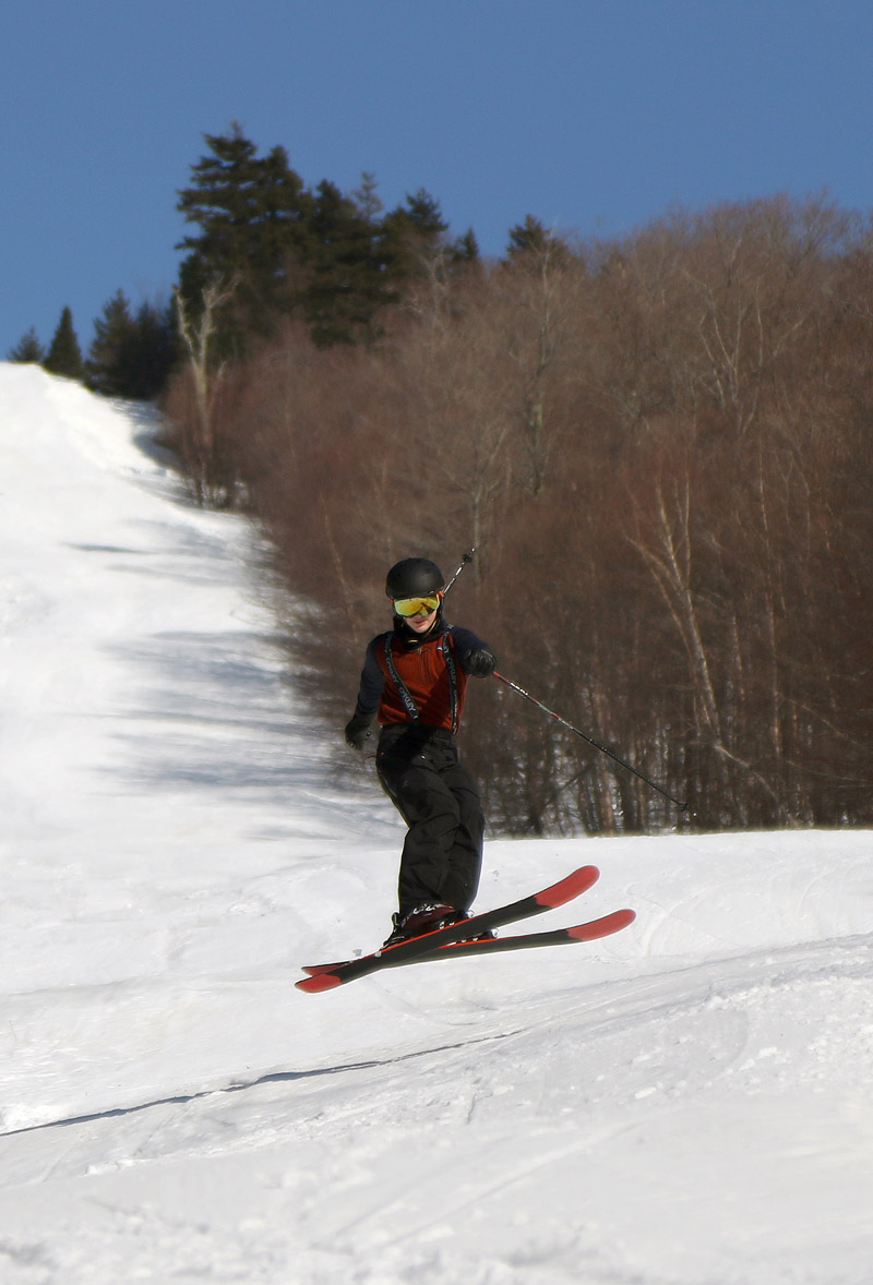An image of Dylan jumping on his skis on the Showtime Trail under the Timberline Quad Chairlift at Bolton Valley Ski Resort in Vermont
