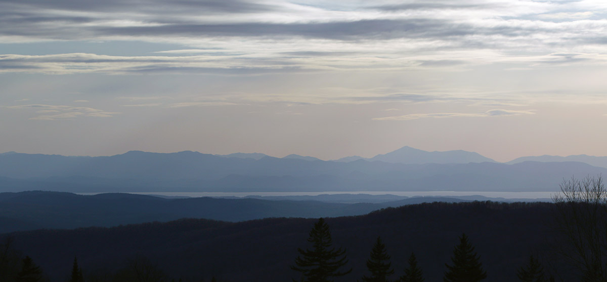 An image showing a view westward toward The Champlain Valley, Lake Champlain, and the Adirondack Mountains of New York during a spring ski tour at Bolton Valley Ski Resort in Vermont