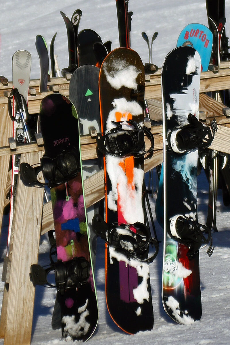 An image of snowboards leaning on a rack in the sun outside the main base lodge on a November ski day at Bolton Valley Ski Resort in Vermont