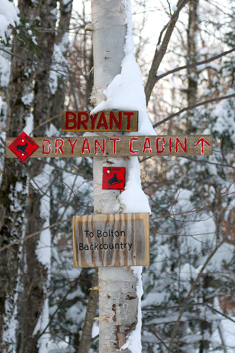 An image of signs for the Bryant Trail, Bryant Cabin, and Bolton Backcountry at the start of a ski tour on the Nordic and Backcountry Network at Bolton Valley Ski Resort in Vermont