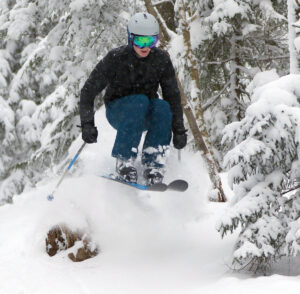 An image of Colin jumping amidst the powder while tree skiing at Bolton Valley Ski Resort in Vermont