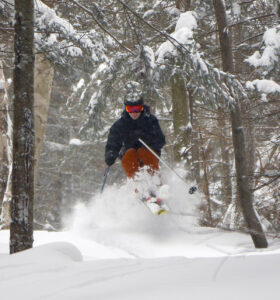 An image of Ty jumping in powder snow in the trees during Winter Storm Quest at Bolton Valley Ski Resort in Vermont