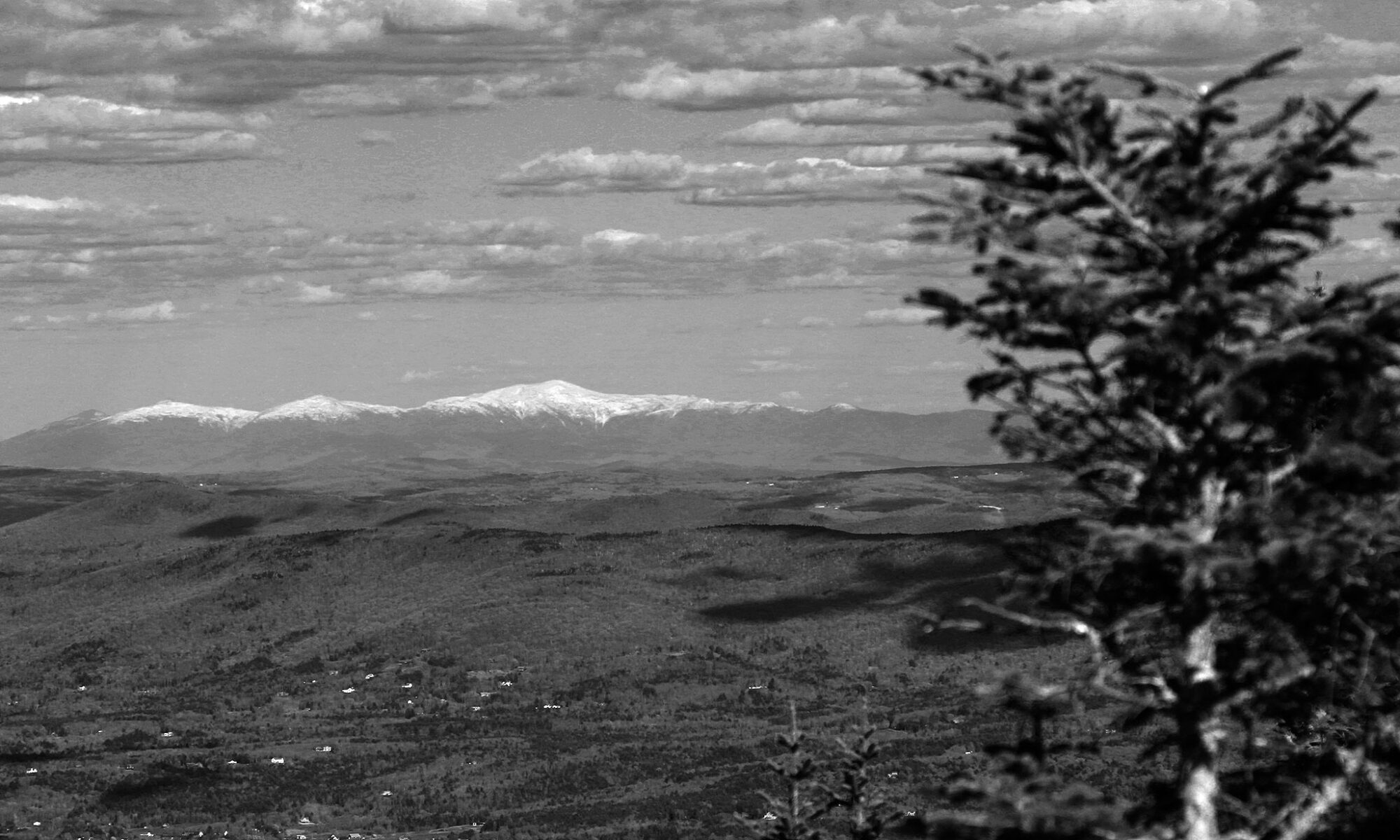A black and white image of the Presidential Range with snow taken in May from Mt. Mansfield in Vermont