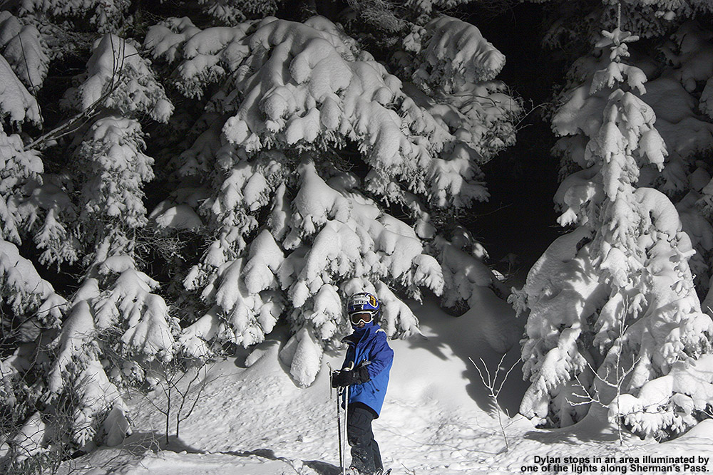 An iamge of Dylan in front of snow-covered evergreens lit up by the night skiing lights at Bolton Valley Resort in Vermont