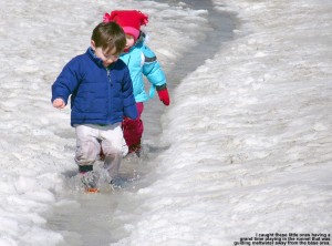 An image of a couple of young children playing in the water in a spring drainage runnel at the base of Bolton Valley Ski Area in Vermont