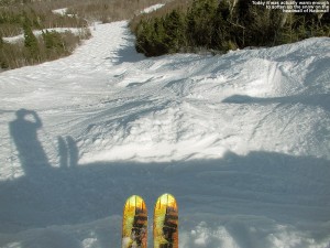 An image of skis poking out over the steep edge of the headwall of the National trail at Stowe Mountain Resort in Vermont, with the steep, snowy, mogul-filled trail below