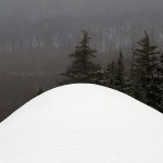 An image looking down a long spine of man made snow atop the headwall of the Spell Binder trail at Bolton Valley Ski Resort in Vermont with trees visible in the background below