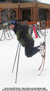 An image of Ken doing a tip stand on his skis outside the Spruce Camp Lodge at Stowe Mountain Resort in Vermont