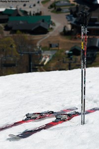 An image of skis and poles on the snow at the top of West Slope at Stowe Mountain Resort in Vermont looking down on the Spruce Peak Base area