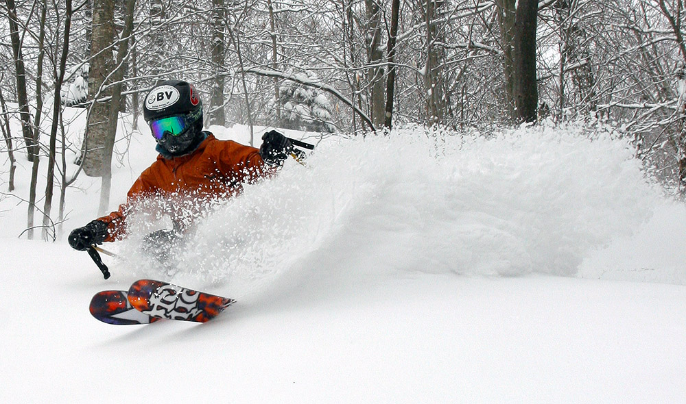 An image of Ty spraying powder while skiing in the trees on Mt. Mansfield at Stowe Mountain Resort in Vermont