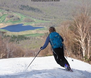 An image of Erica skiing on the slopes of Mt. Mansfield at Stowe Mountain Resort in Vermont in Mid May with an image of a pond and spring foliage in the background