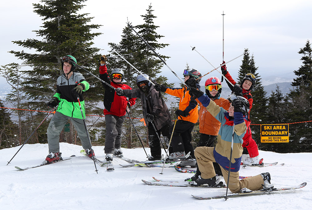 An image of students from the Bishop John A Marshall School raising their ski poles as they get ready for a run down the Bruce Trail outside the boundaries of Stowe Mountain Ski Resort in Vermont