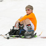 An image of Dylan sitting on the snow at the start of spring skiing ascent at Stowe Mountain Resort in Vermont