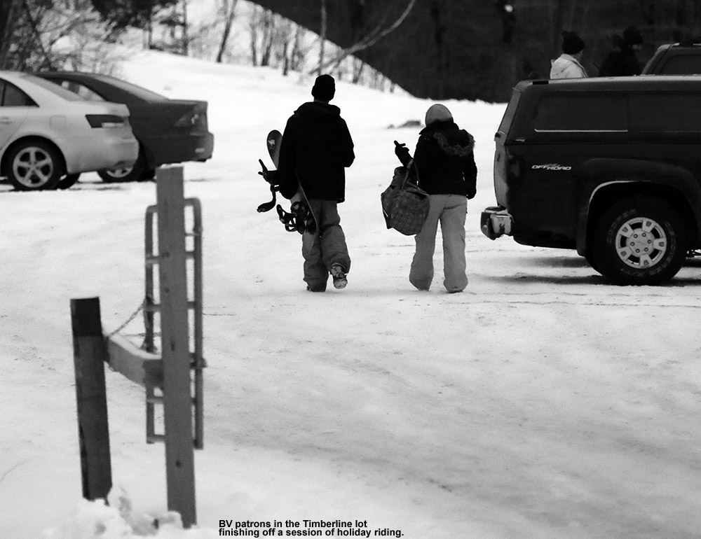 An image of a snowboarder and companion heading to their vehicle in the Timberline parking area at Bolton Valley Ski Resort in Vermont