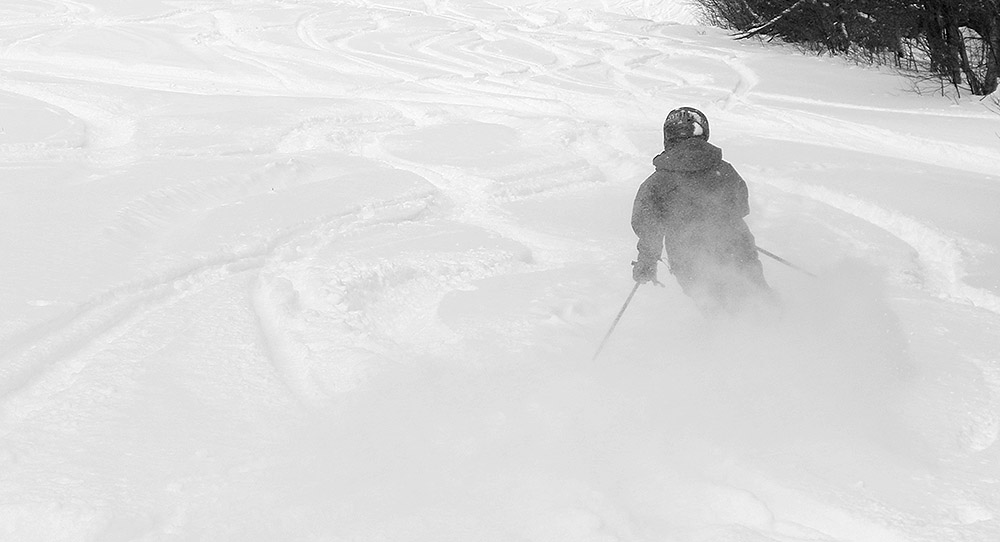 An image from behind of Ty skiing powder on the Tattle Tale trail at Bolton Valley Resort in Vermont