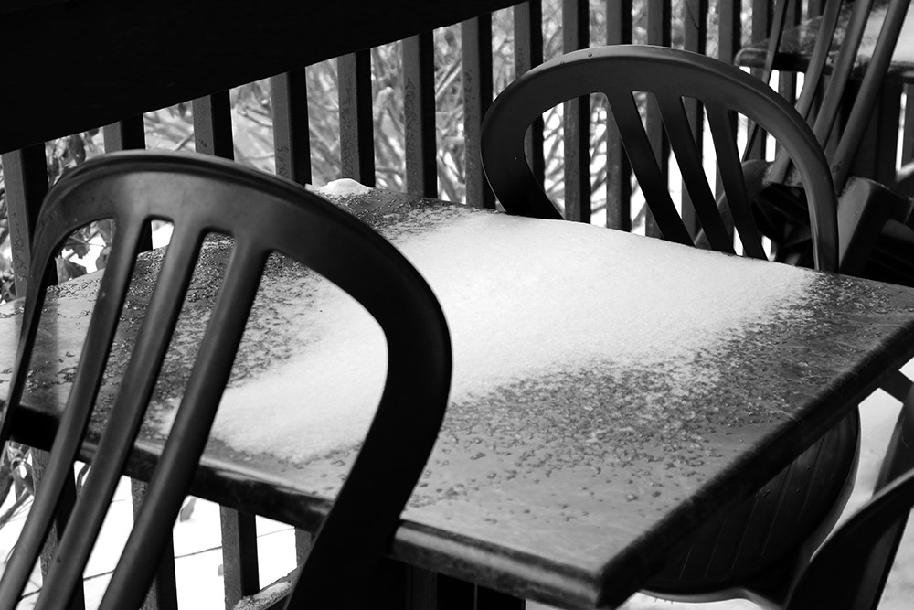 An image of snowy chairs on the deck in front of the Deli in the Bolton Valley Village at Bolton Valley Ski Resort in Vermont