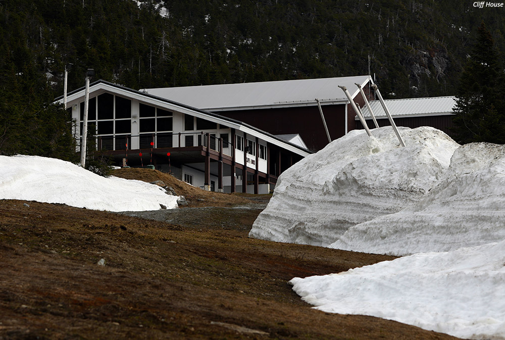 An image of deep snow piles in May up on Mt. Mansfield at the Cliff House after work road plowing by Stowe Mountain Ski Resort in Vermont