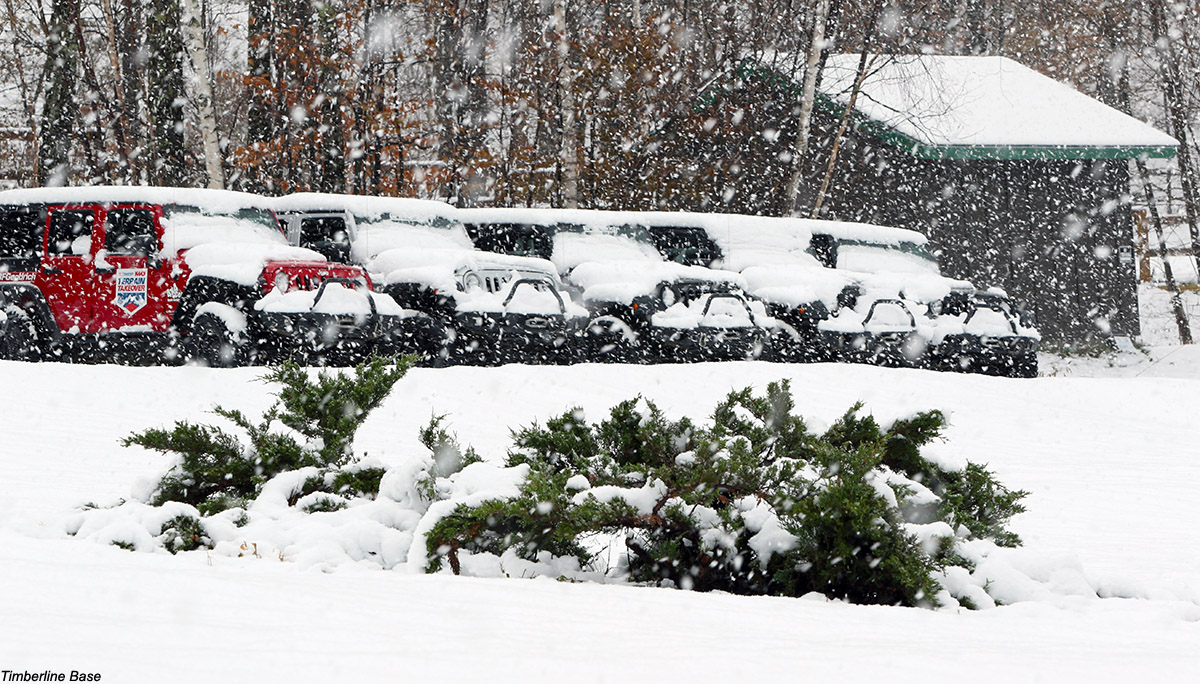 An image showing some of the four-wheel drive vehicles parked at the Timberline base area of Bolton Valley Resort in Vermont as heavy snowfall fills the arir from a November snowstorm