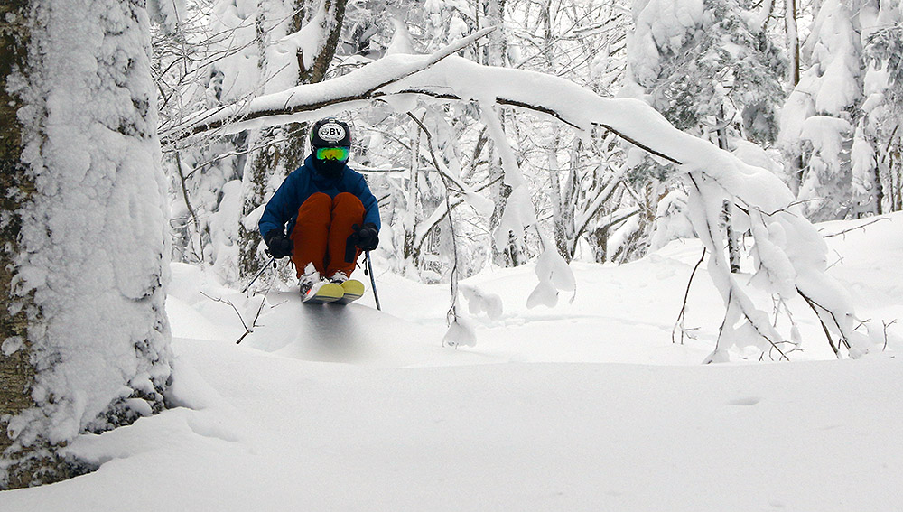 An image of Ty skiing powder and ducking under a bent tree in the Snow Hole area of Bolton Valley Resort in Vermont