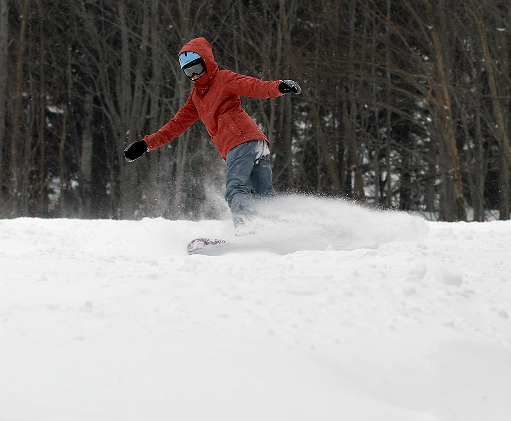 An image of Molly snowboarding in powder on the Upper Meadows trail at Stowe Mountain Resort in Vermont