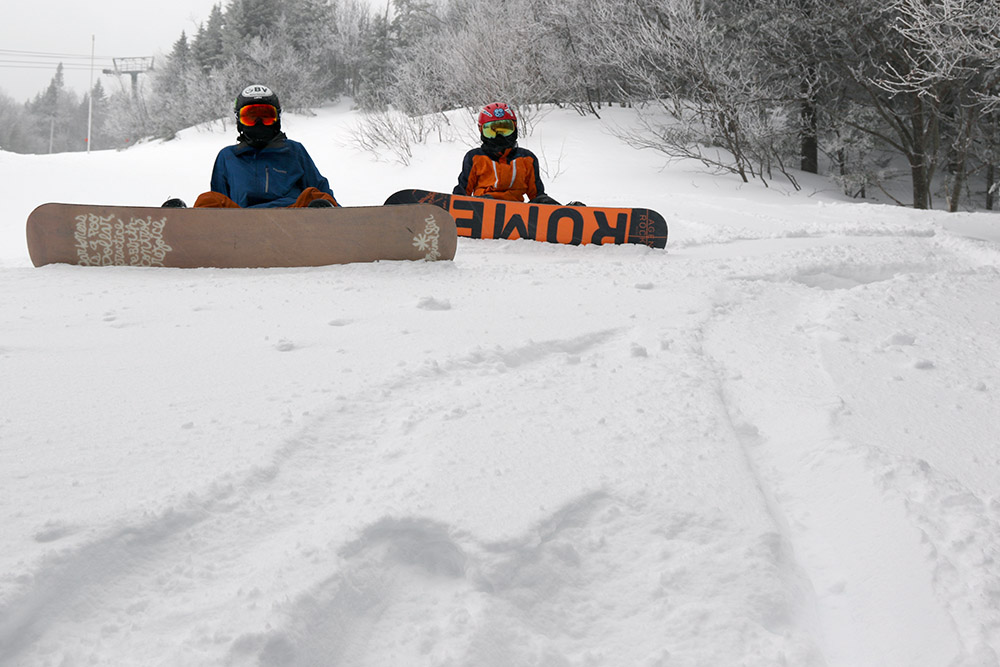 An image of Ty and Dylan on snowboards along the edge of the Switchback trail at Stowe Mountain Resort in Vermont