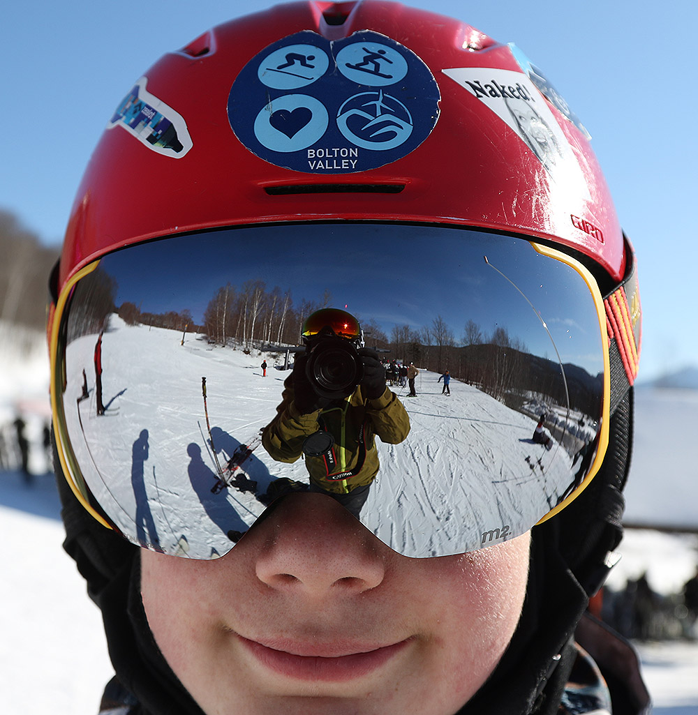 An image of Dylan wearing a silver ski goggle lens on a sunny day at the Timberline Base of Bolton Valley Ski Resort in Vermont