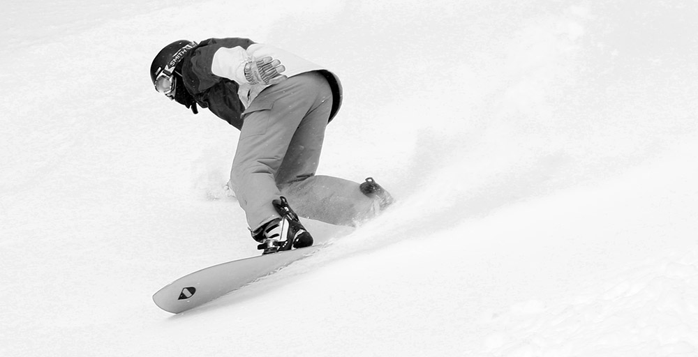 An image of a snowboarder riding in powder snow near the sumit of Spruce Peak at Stowe Mountain Resort in Vermont