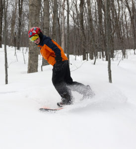 An image of Dylan snowboardinig in powder from the back side of Winter Storm Ulmer in the Toll House Trees at Stowe Mountain Resort in Vermont