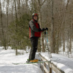 An image of Brian showing the four to five foot snowpack that is level with the railings of a bridge along the Ranch Brook in the Mt. Mansfield sidecountry near Stowe Mountain Resort in Vermont