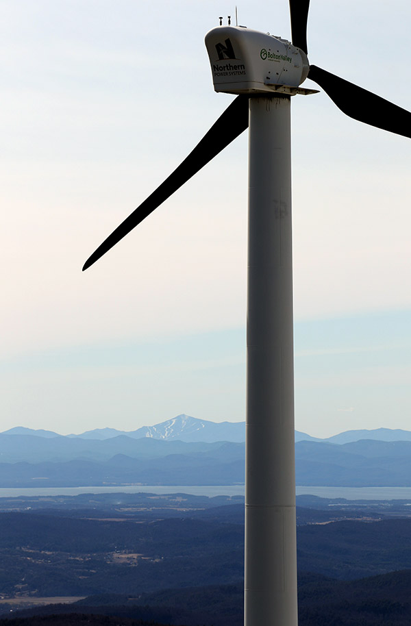 An image of the Bolton Valley wind turbine with Lake Champlain and Whiteface Mountain taken from the Vista Peak Fire Tower at Bolton Valley Resort in Vermont