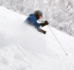 An image of Erica spraying powder snow from Winter Storm Odell as she skis at Bolton Valley Resort in Vermont