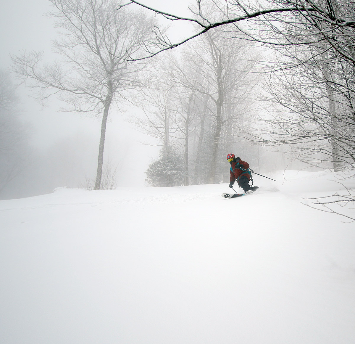 A wide-angle image of Dylan skiing in powder from Winter Storm Quincy out on a ski tour at Bolton Valley Resort in Vermont