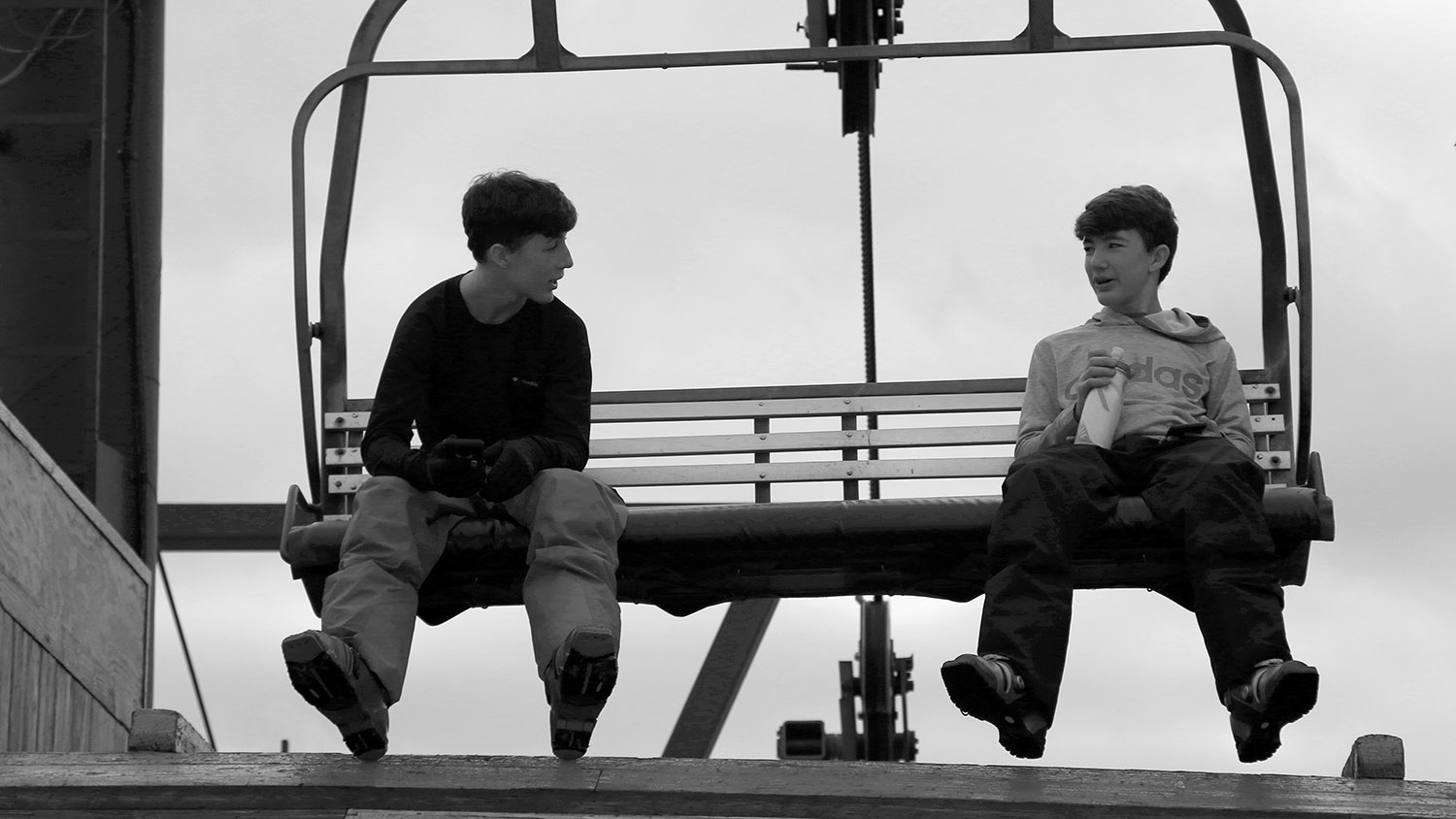 An image of Ty and Dylan on a chair of the Timberline Quad Chairlift during a ski tour at Bolton Valley Resort in Vermont.