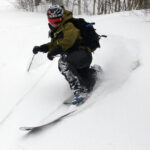 A close-up, wide-angle image of Jay Telemark skiing in powder during an April snowstorm at Bolton Valley Ski Resort in Vermont