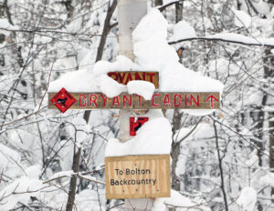 An image of a snow-covered sign indicating one of the entrances to the backcountry and trail information at Bolton Valley Ski Resort in Vermont