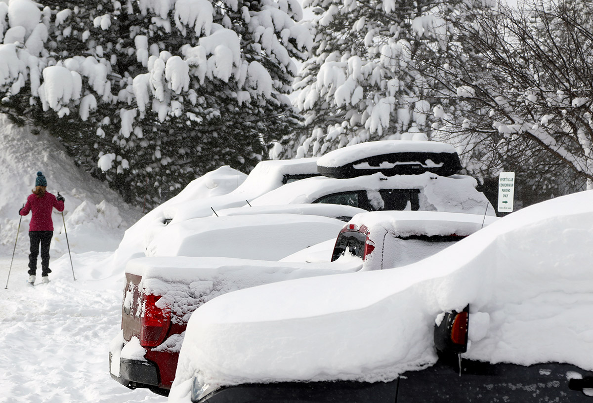 A snowy scene with a skier and cars from the Village area of Bolton Valley Ski Resort in Vermont after some January snowstorms