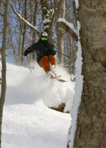 An image of Ty dropping off a ledge while powder skiing after Winter Storm Roland at Bolton Valley Ski Resort in Vermont