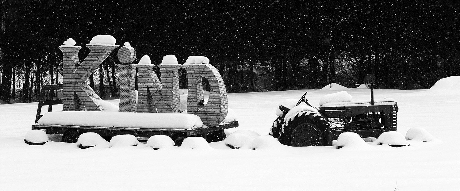 An image of a tractor pulling a sled in the snow with the word "KIND" spelled out among midwinter snow in the Waterbury Center area of Vermont