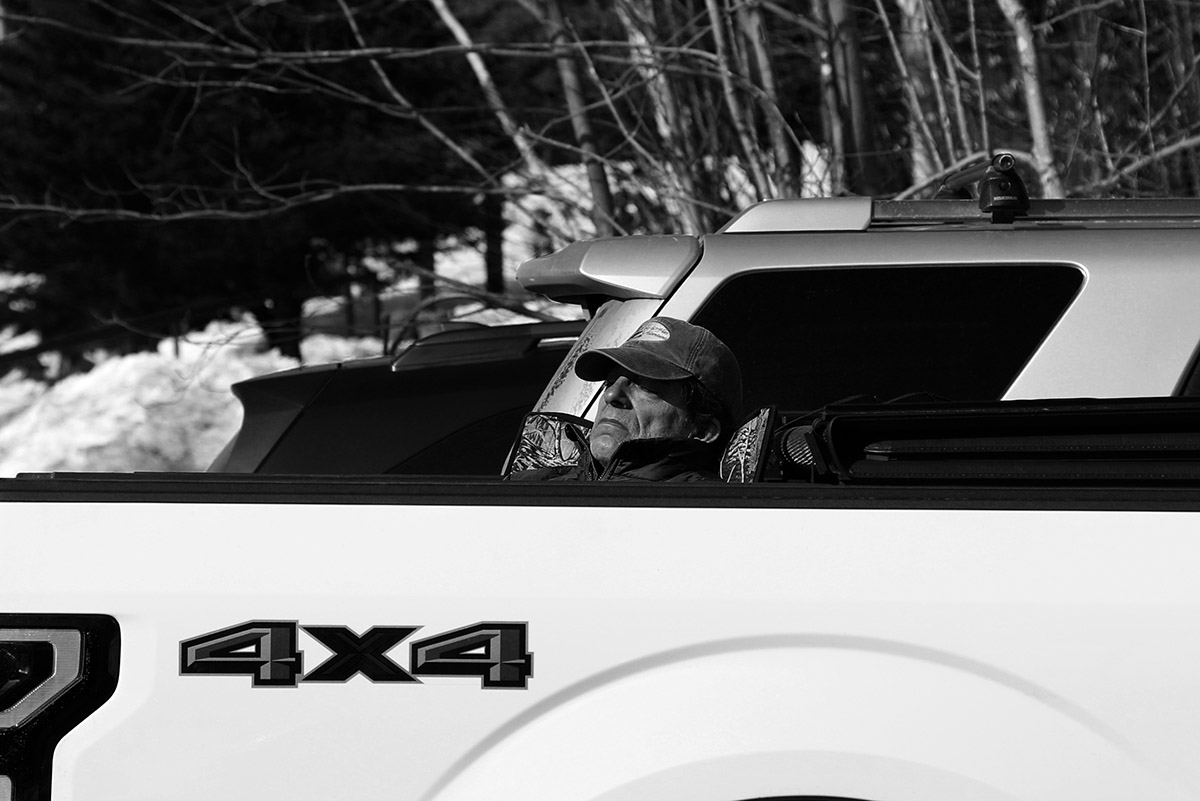 An image of a man napping in the sun in the back of his pickup truck at the Timberline Base area of Bolton Valley Ski Resort in Vermont