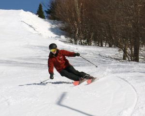 An image of Dylan carving on his skis in soft spring snow on the Showtime trail under the Timberline Quad Chairlift at Bolton Valley Ski Resort in Vermont