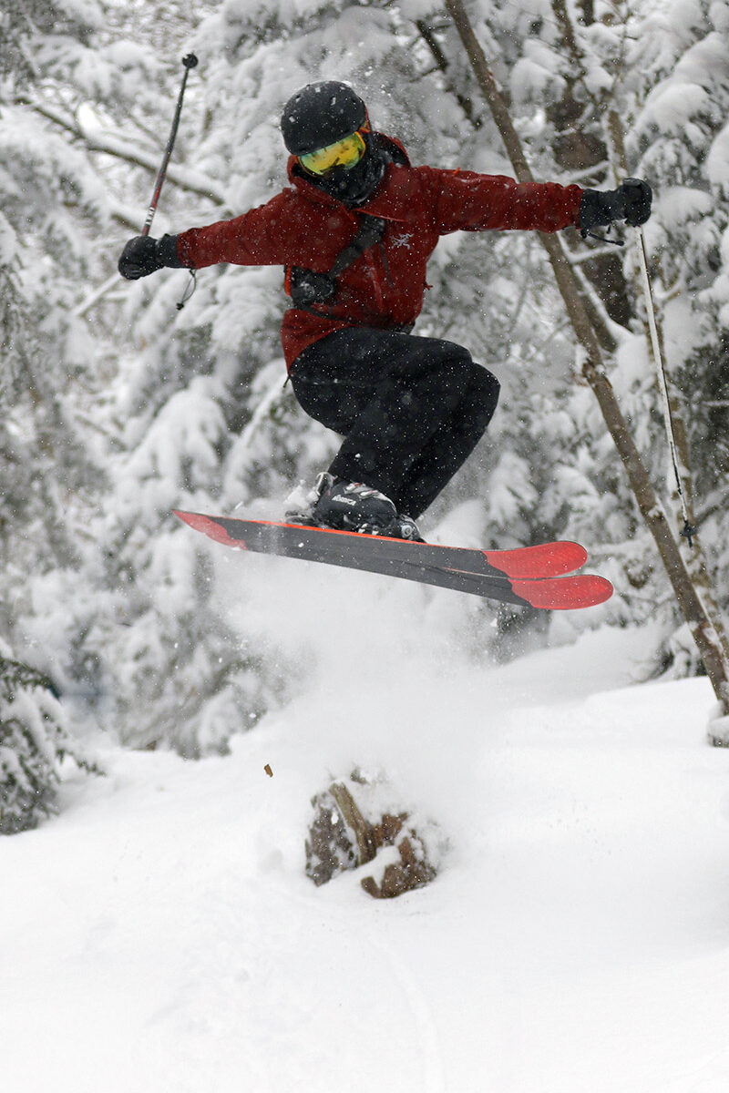 An image of Dylan performing a twisting jump among the powder while skiing in the trees at Bolton Valley Ski Resort in Vermont