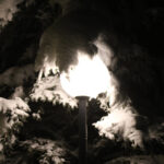 A night image of a light covered by snowy evergreen boughs from recent early December snowfall in the Village area of Bolton Valley Ski Resort in Vermont
