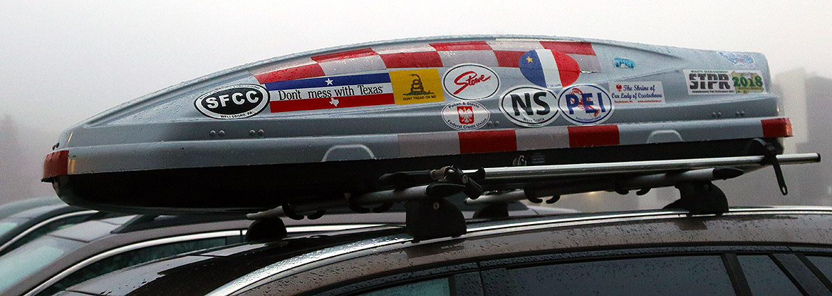 An image of a car roof top cargo box with stickers from various locations in North America located in one of the parking lots of the Village during the Christmas holiday week at Bolton Valley Ski Resort in Vermont