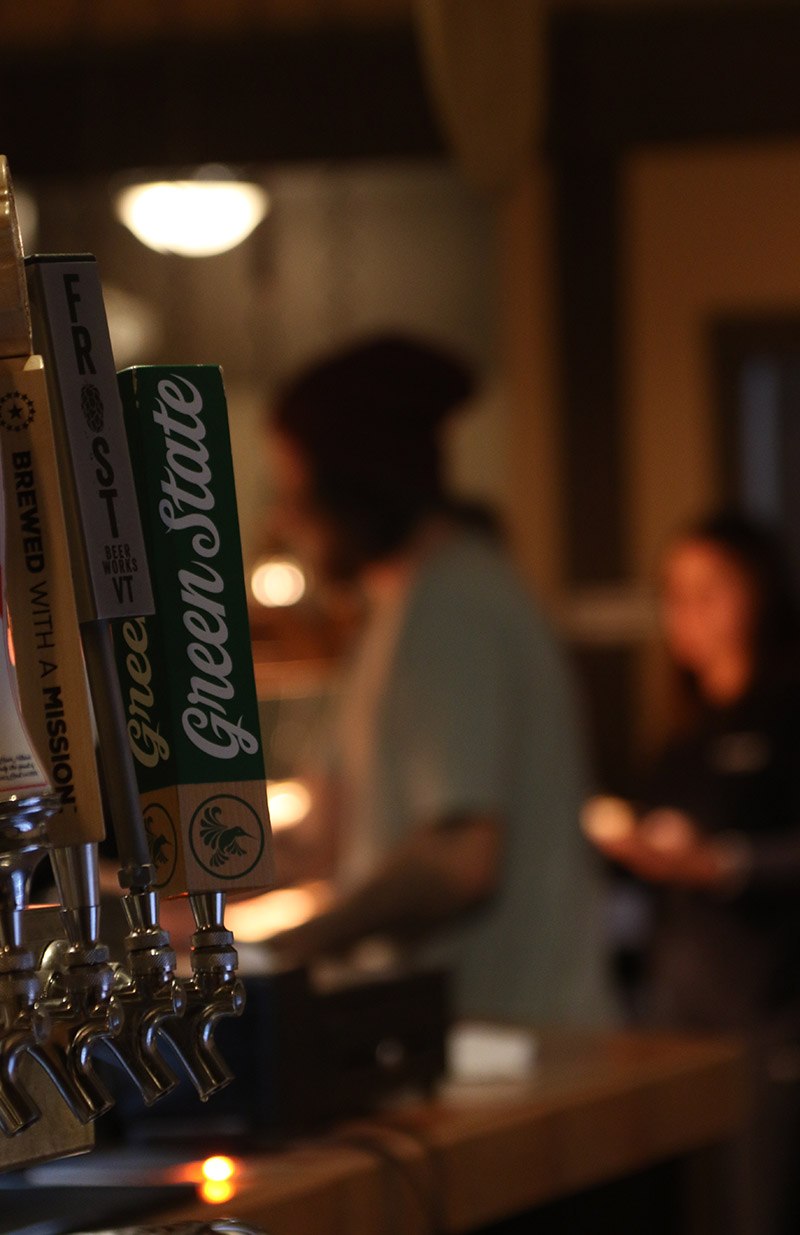 An image of beer taps with pizza in the background showing the Fireside Flatbread restaurant at Bolton Valley Ski Resort in Vermont
