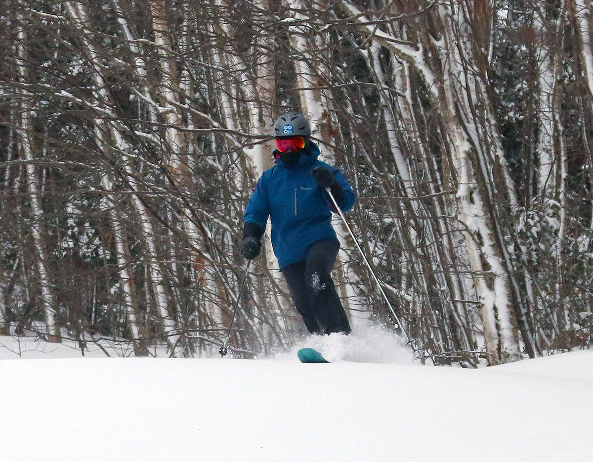 An image of Erica making Telemark turns in untracked powder snow on the Snowflake Bentley trail with birch trees in the background after Winter Storm Gerri at Bolton Valley Ski Resort in Vermont