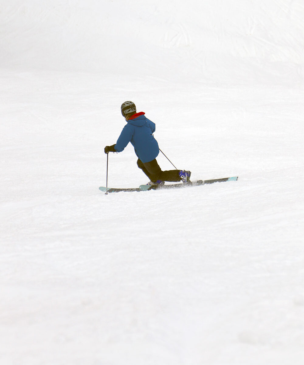 An image of Erica Telemark skiing in soft snow during a warm February day on the Spell Binder trail in the Timberline area at Bolton Valley Ski Resort in Vermont