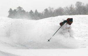 An image of Dylan skiing through a cloud of powder during a late winter storm at Bolton Valley Ski Resort in Vermont