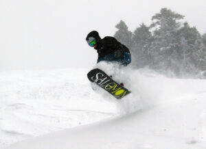 An image of Colin jumping on his snowboard amidst a cloud of powder snow during a March winter storm at Bolton Valley Ski Resort in Vermont