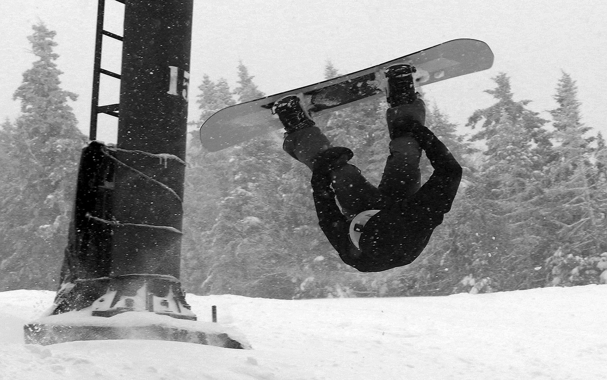 An image of Colin on his snowboard inverted during a back flip off one of the jumps on the Intro trail during a big spring snowstorm at Bolton Valley Ski Resort in Vermont